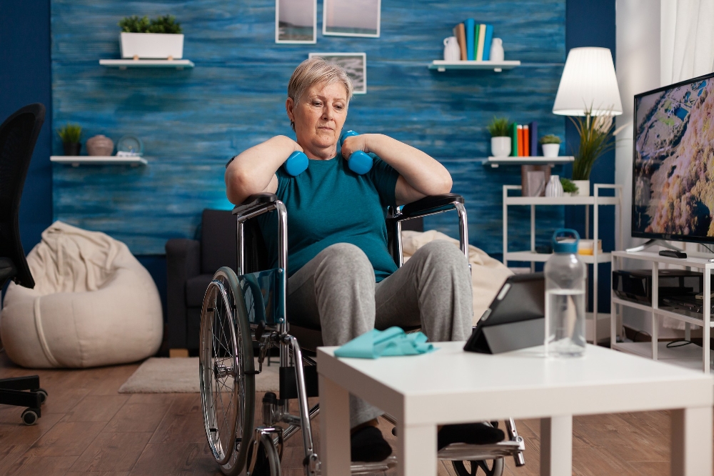 Older woman in a wheelchair lifting blue dumbbells at home, an exercise scene related to living with rheumatoid arthritis